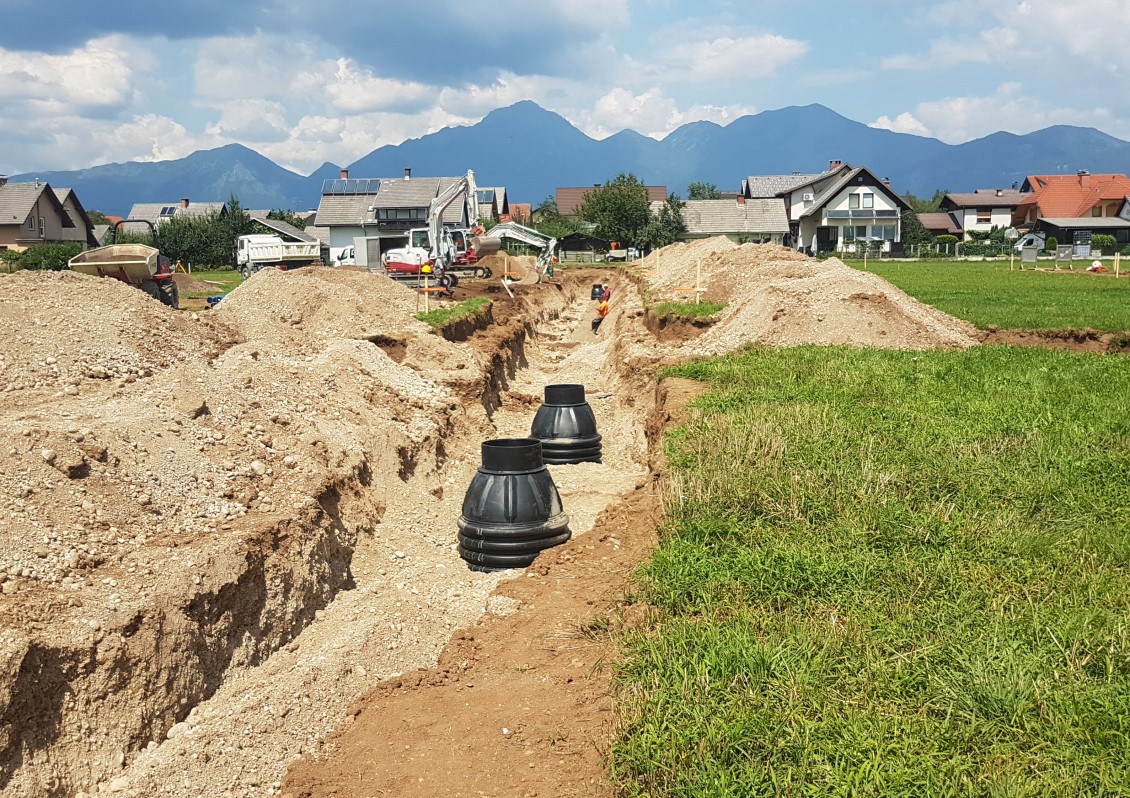 Construction site with trenches and pipes surrounded by houses and mountains